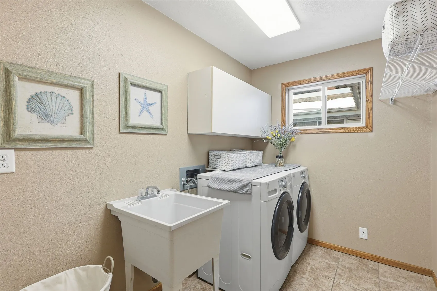 Spacious laundry room complete with utility sink, cabinets, shelving and some natural light.