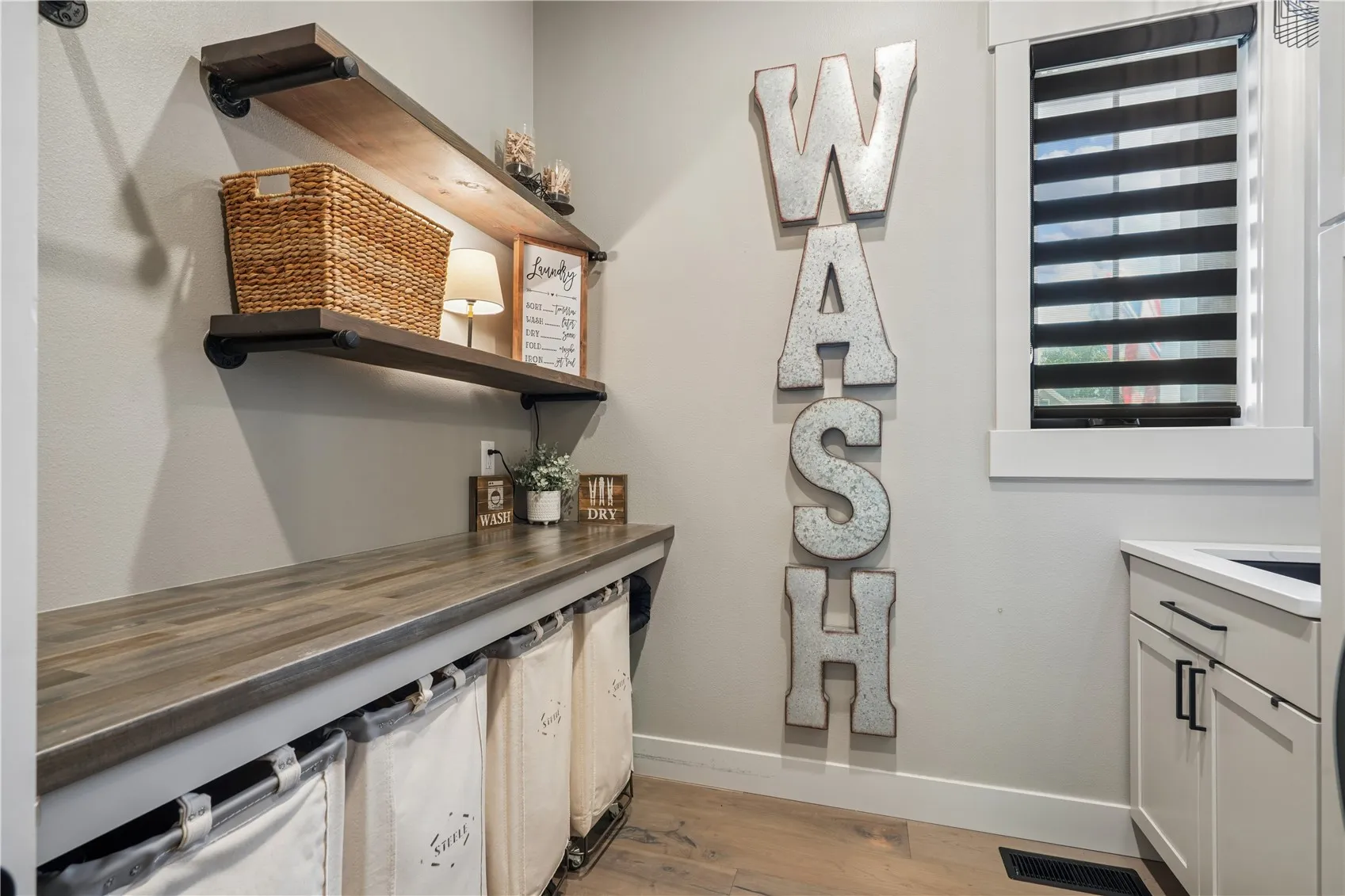 Main floor laundry features a folding counter, clothing bar, sink and cabinetry. Window with custom blinds.