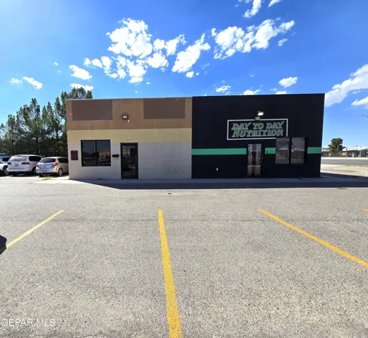 Commercial building featuring a flat roofline, multiple storefront entrances, window displays, and an asphalt parking lot with striped spaces