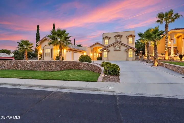 Stucco exterior with multiple dormer windows, a concrete driveway, and mature palm trees