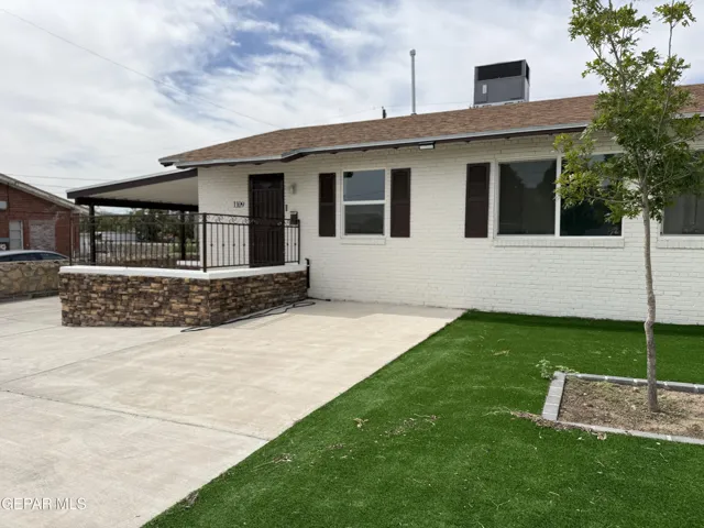 White brick exterior with dark shutters, covered front patio, stone facade, wrought iron railing, and a concrete driveway