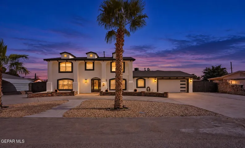 Stucco exterior with contrasting trim, arched entry, prominent garage with horizontal detailing, concrete driveway, and rock landscaping