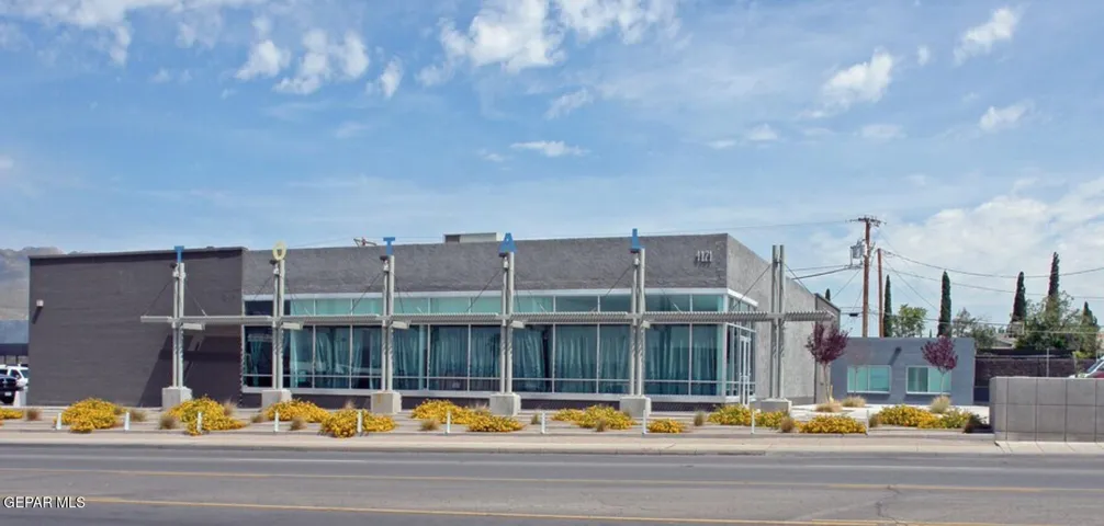 Contemporary commercial building featuring a flat roof and extensive window frontage, complemented by decorative exterior beams and integrated landscaping