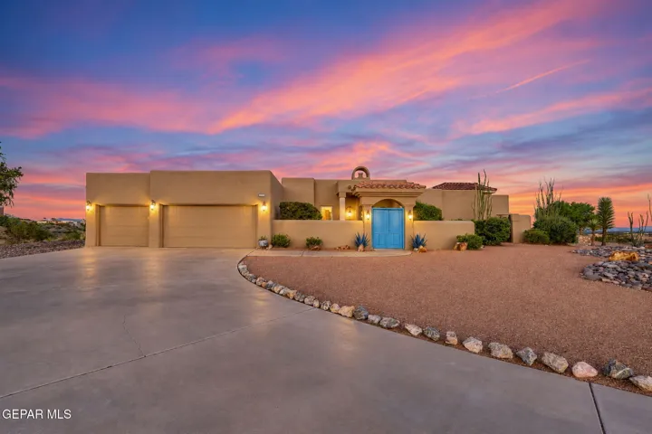 Stucco exterior with a tiled entry arch, triple garage bays, a stone-lined gravel front yard, and a concrete driveway