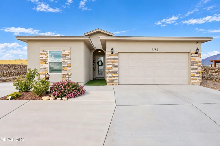 Stucco exterior with stone accents, attached two-car garage, concrete driveway, arched entry, and low-maintenance landscaping