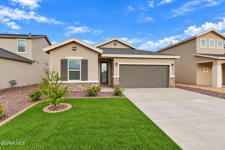 Stucco exterior with stone accents, attached garage, well-maintained lawn, and established landscaping