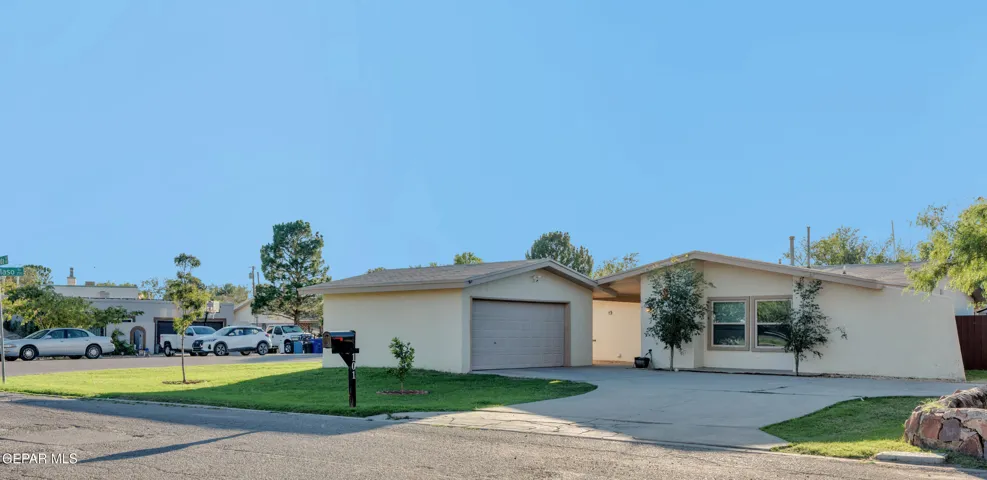 Single-story exterior featuring light-toned stucco siding, a concrete driveway, an attached garage, and a grass lawn