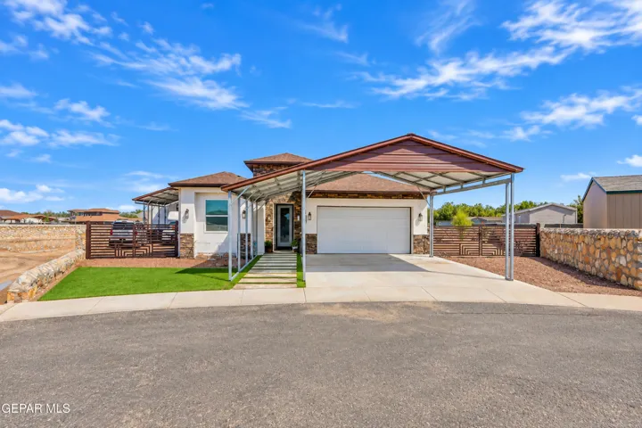 Modern manufactured home featuring a covered front porch, white horizontal siding, a two-car garage with overhead door, and manicured landscaping with mature grass lawn