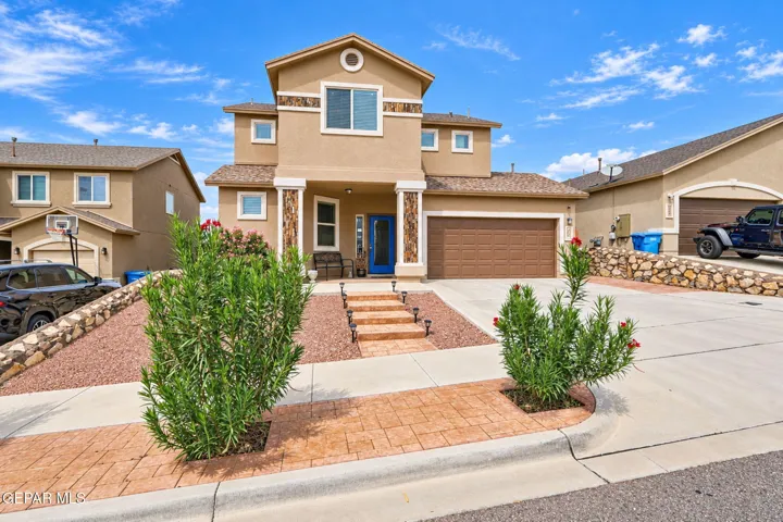 Stucco exterior with stone accents, attached garage, concrete driveway, stamped concrete walkway, and landscaped front yard