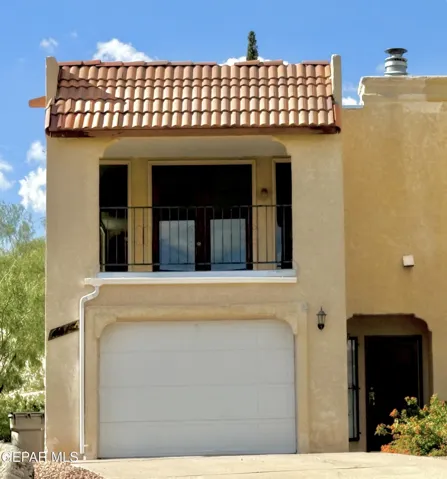 Stucco exterior featuring a terracotta tile roof, second-story balcony with metal railing, and an attached garage with a panel door