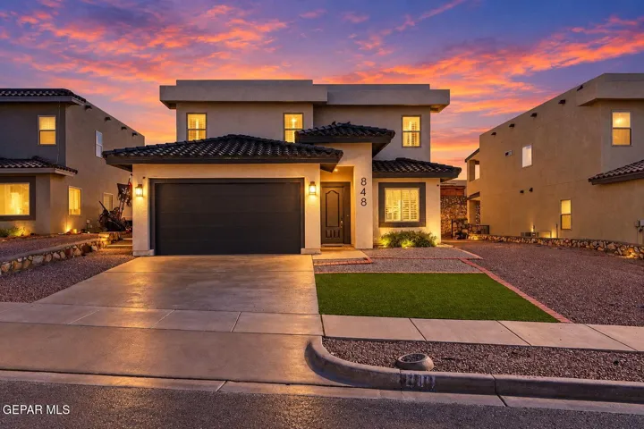 Stucco exterior residence featuring a tile roof, an attached two-car garage, and low-maintenance landscaping