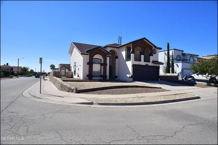 Two-story residence featuring a stucco exterior, arched masonry detailing, a second-story balcony, and a stone-walled xeriscape front yard