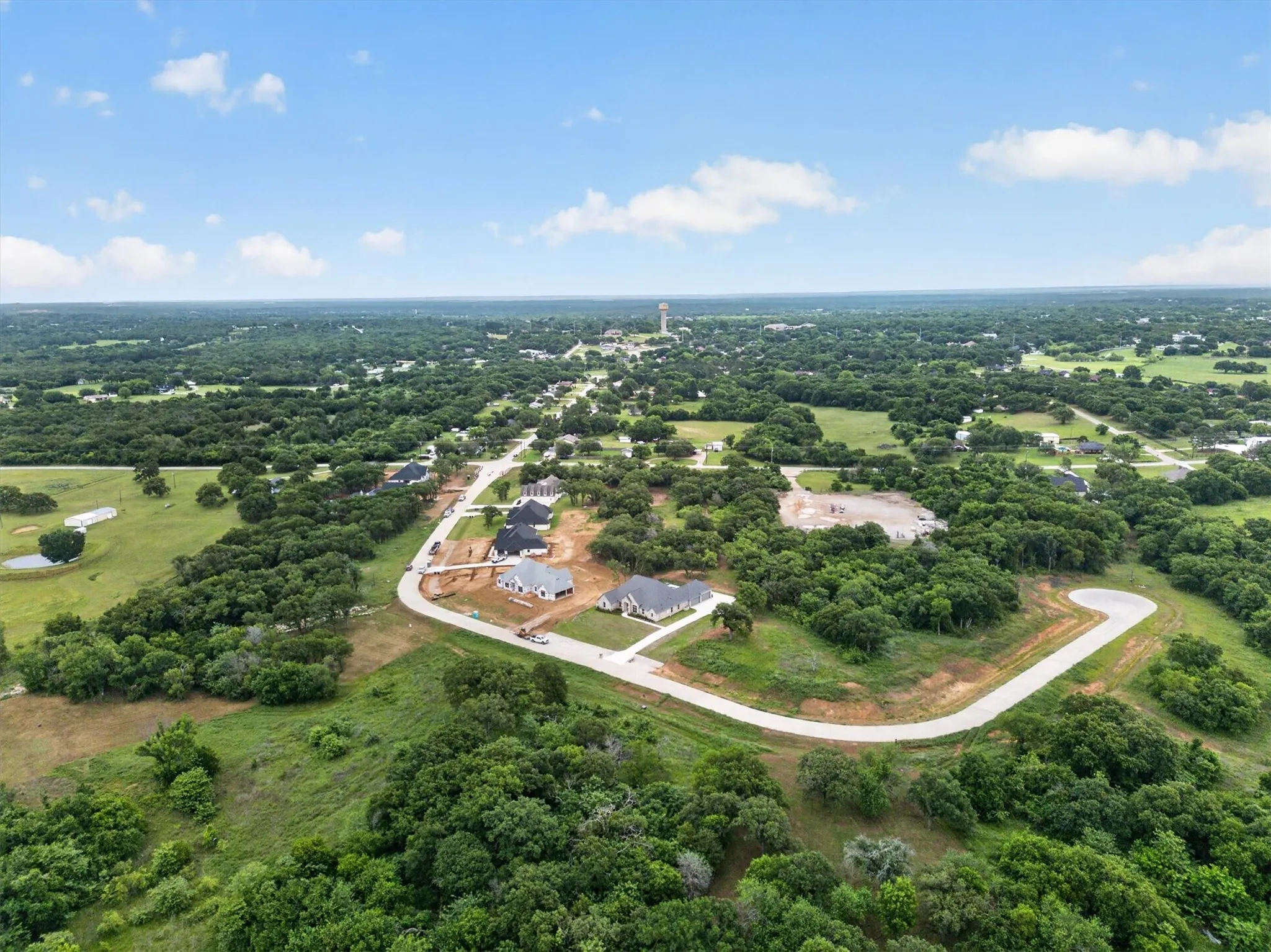 Expansive aerial showcasing a developing residential area surrounded by abundant mature trees and verdant landscapes