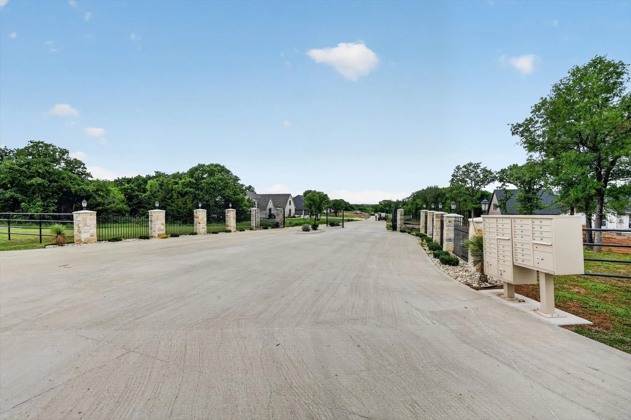 Paved entry drive with stone pillars, black metal fencing, and integrated lighting