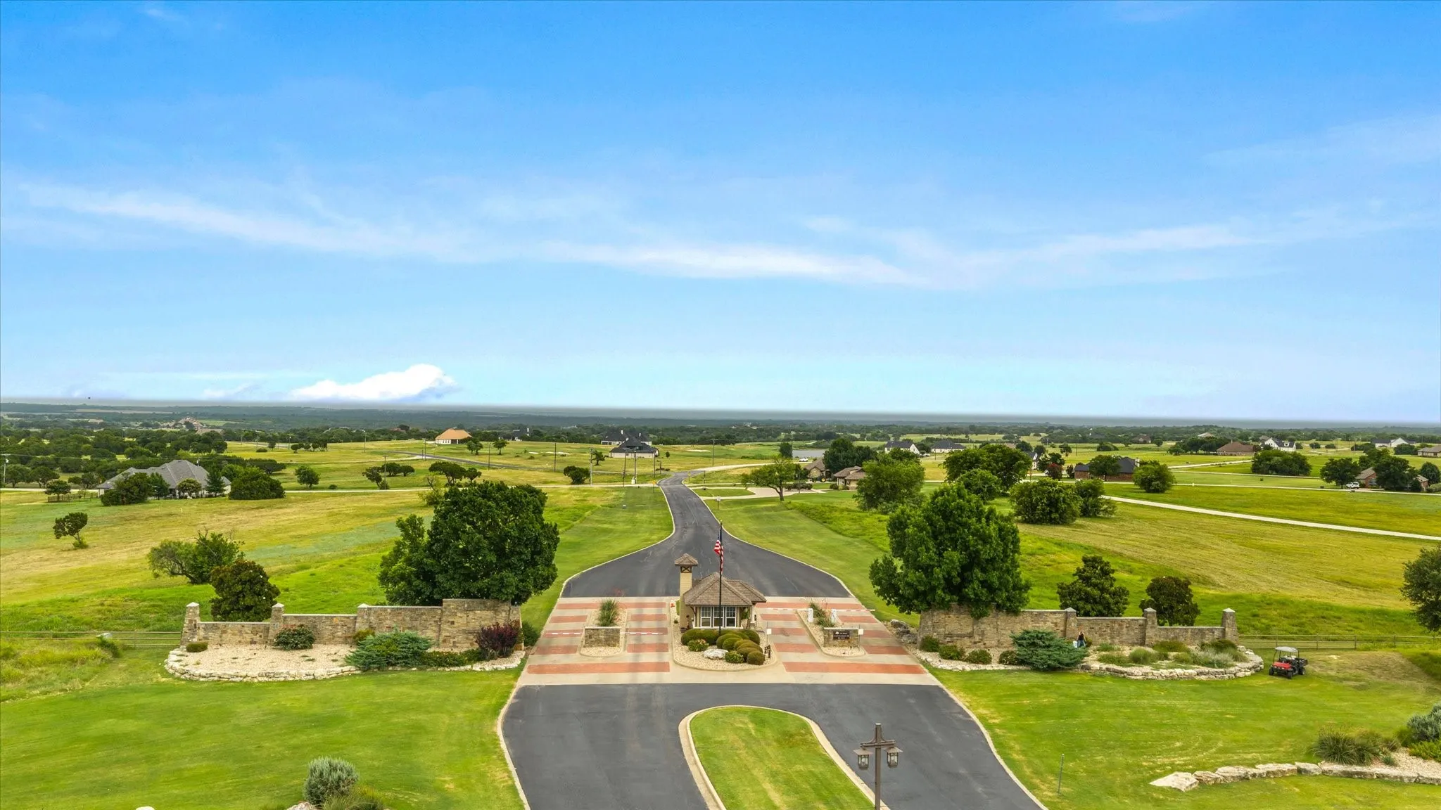 Gated entrance featuring stone walls, mature landscaping, and an expansive paved driveway