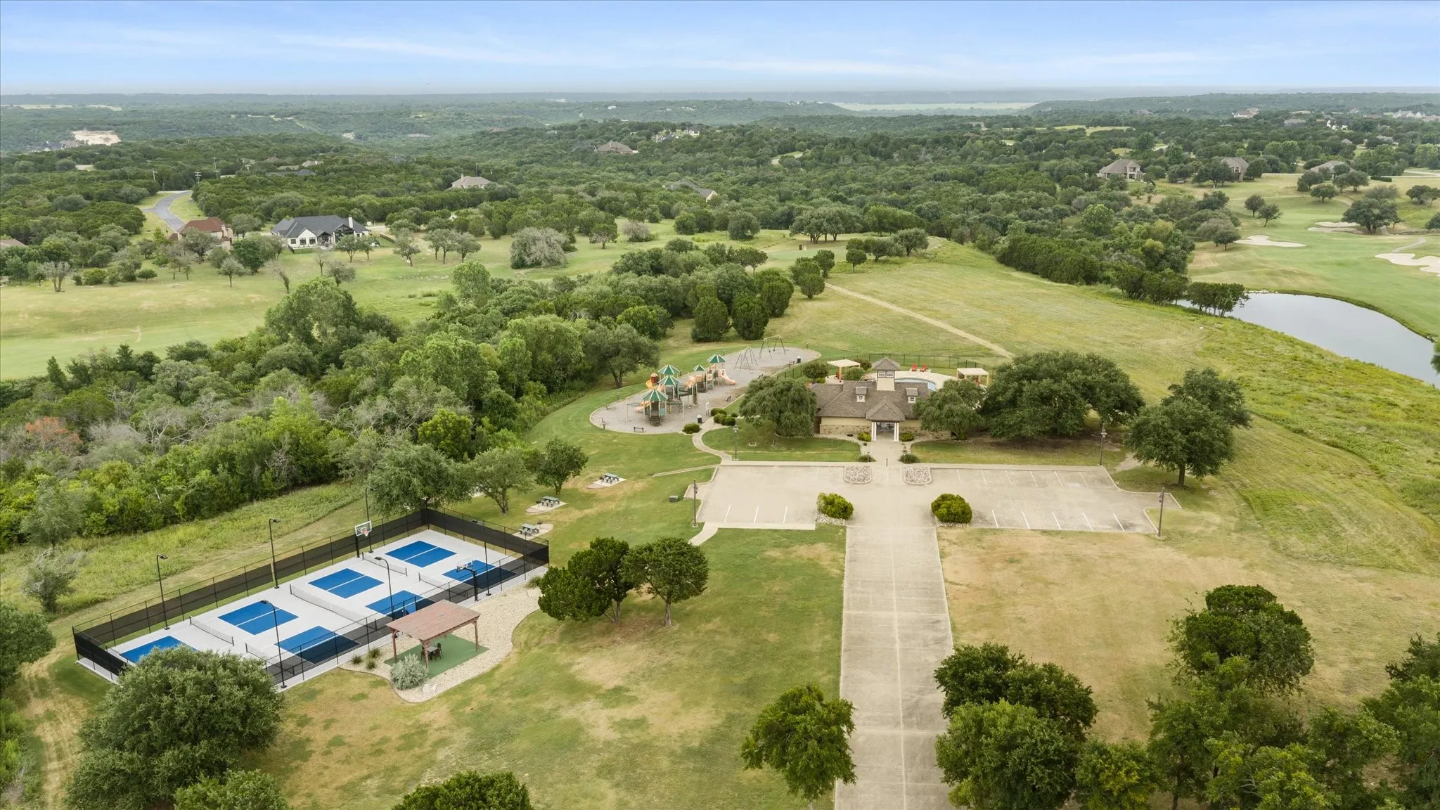 Community recreational area featuring multiple pickleball courts, a central clubhouse building, a playground, and ample parking