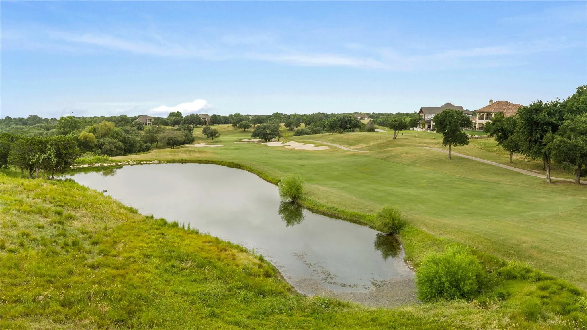 Expansive golf course property featuring a pond, manicured fairways, mature trees, and multiple residential structures in the background