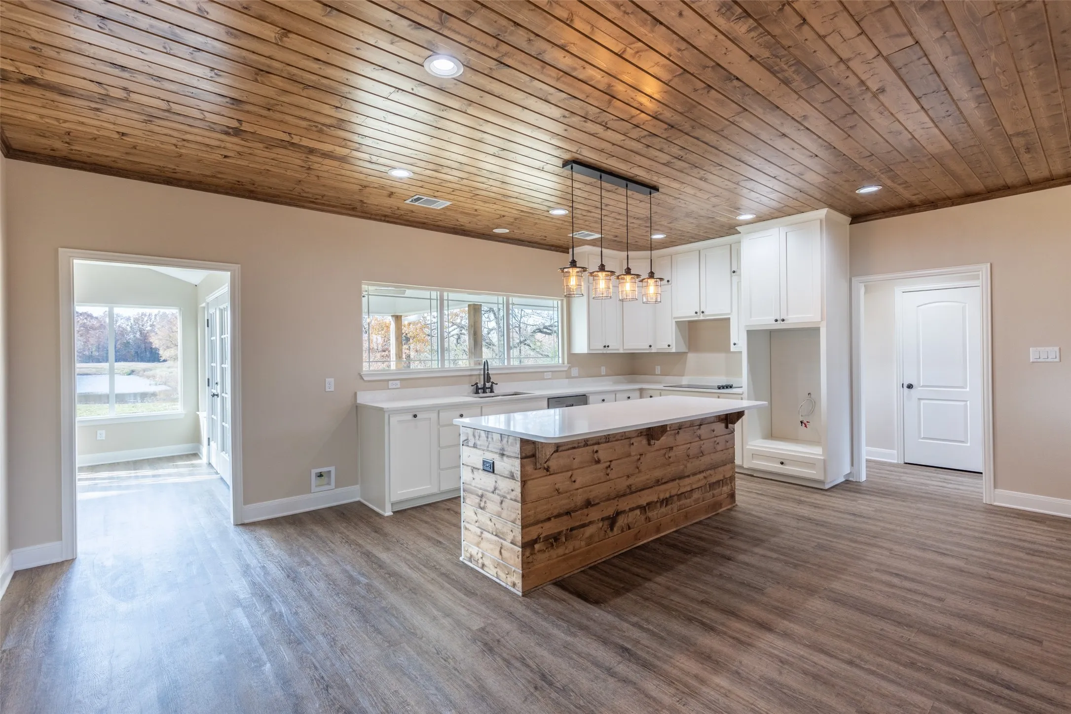 Example Photos: Kitchen featuring a substantial island with a wood-finish base, white cabinetry, quartz countertops, a multi-light pendant fixture, and a wood-plank ceiling