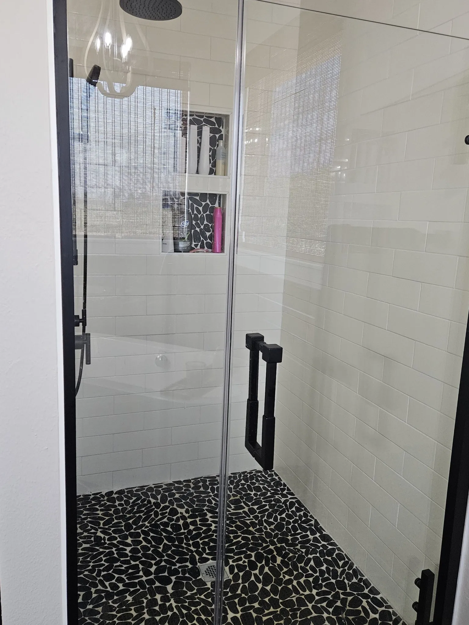 Example Photos: Glass-enclosed shower featuring a black pebble floor, white subway tile walls, and dual recessed niches with patterned tile accents