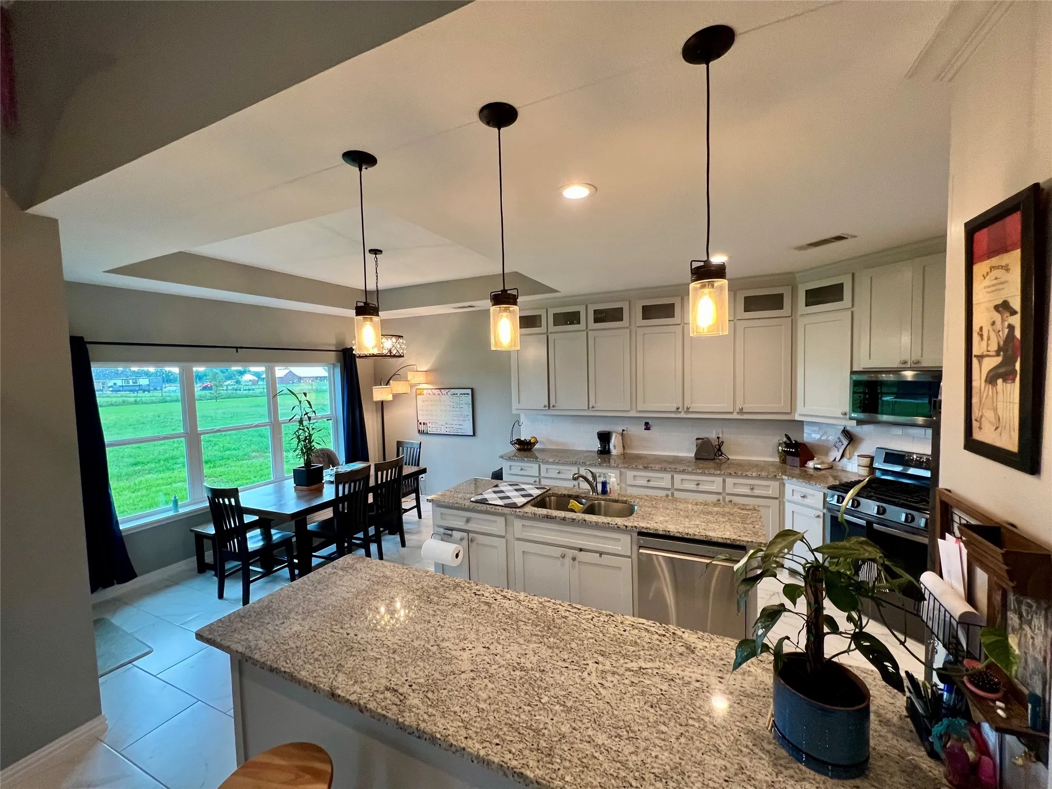 Kitchen featuring a tray ceiling, stainless steel appliances, light tile flooring, decorative light fixtures, and white cabinets