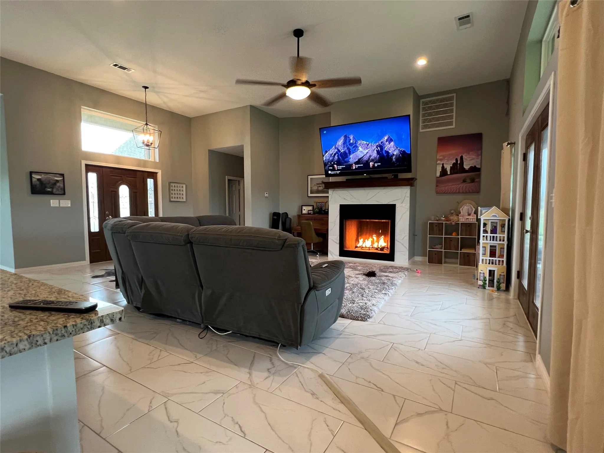 Living room with tile flooring, a high end fireplace, and ceiling fan with notable chandelier