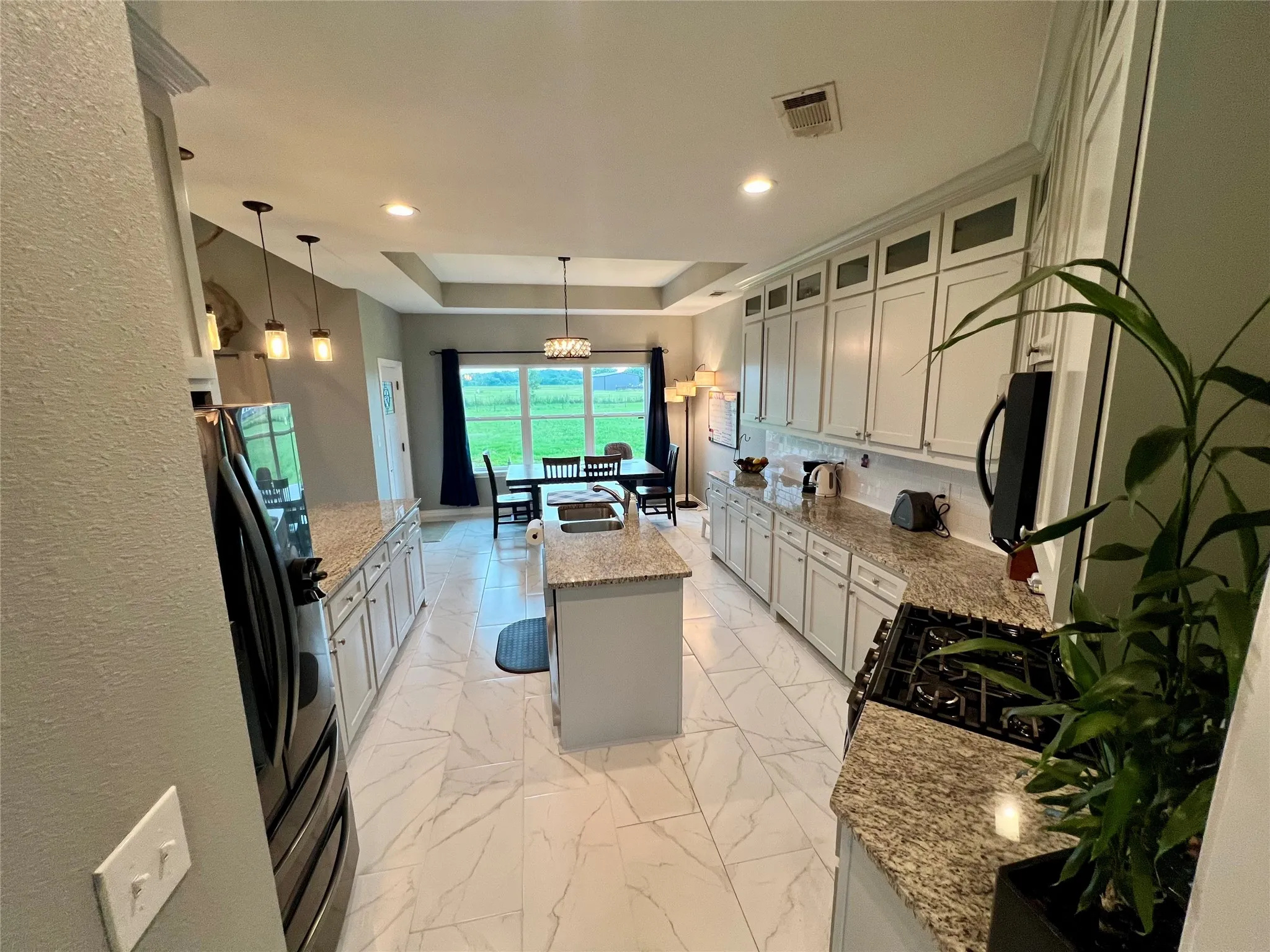 Kitchen featuring decorative light fixtures, a kitchen island, a tray ceiling, light stone countertops, and sink