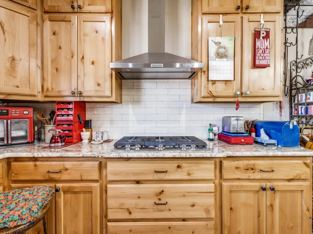 Kitchen with backsplash, stainless steel gas stovetop, light stone countertops, and wall chimney range hood