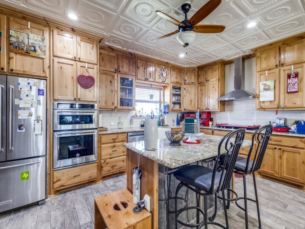 Kitchen featuring wall chimney exhaust hood, appliances with stainless steel finishes, light stone counters, a kitchen island, and light hardwood / wood-style floors