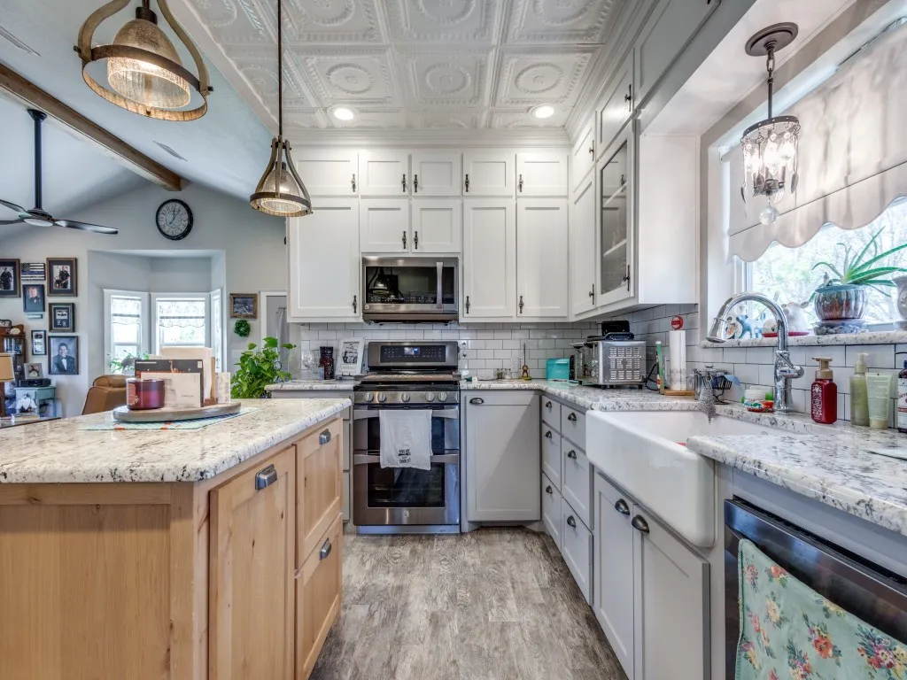 Kitchen featuring decorative light fixtures, white cabinets, light stone countertops, stainless steel appliances, and tasteful backsplash