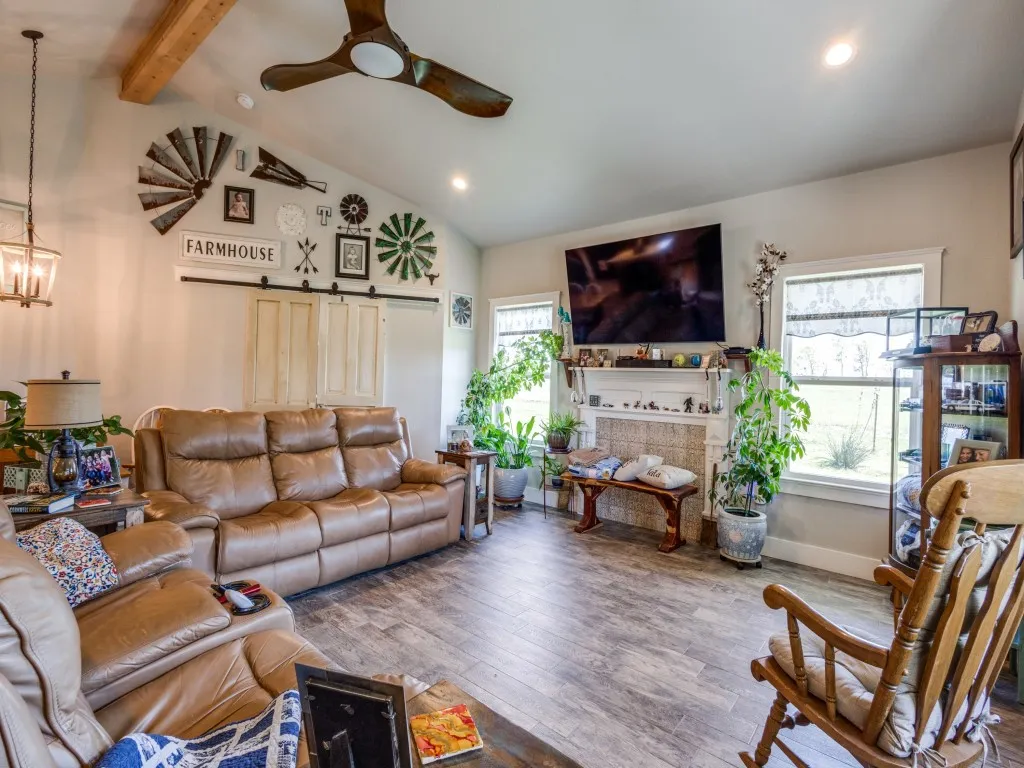 Living room featuring high vaulted ceiling, beamed ceiling, ceiling fan with notable chandelier, dark wood-type flooring, and a tile fireplace