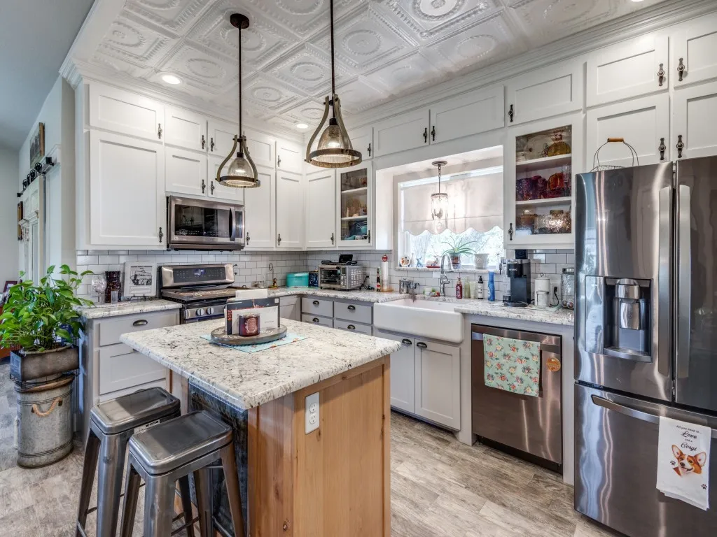 Kitchen featuring appliances with stainless steel finishes, backsplash, hanging light fixtures, white cabinets, and a center island