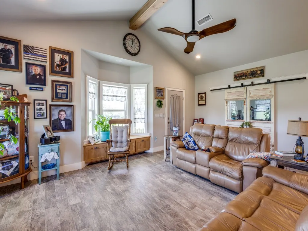 Living room with high vaulted ceiling, beam ceiling, ceiling fan, and light hardwood flooring