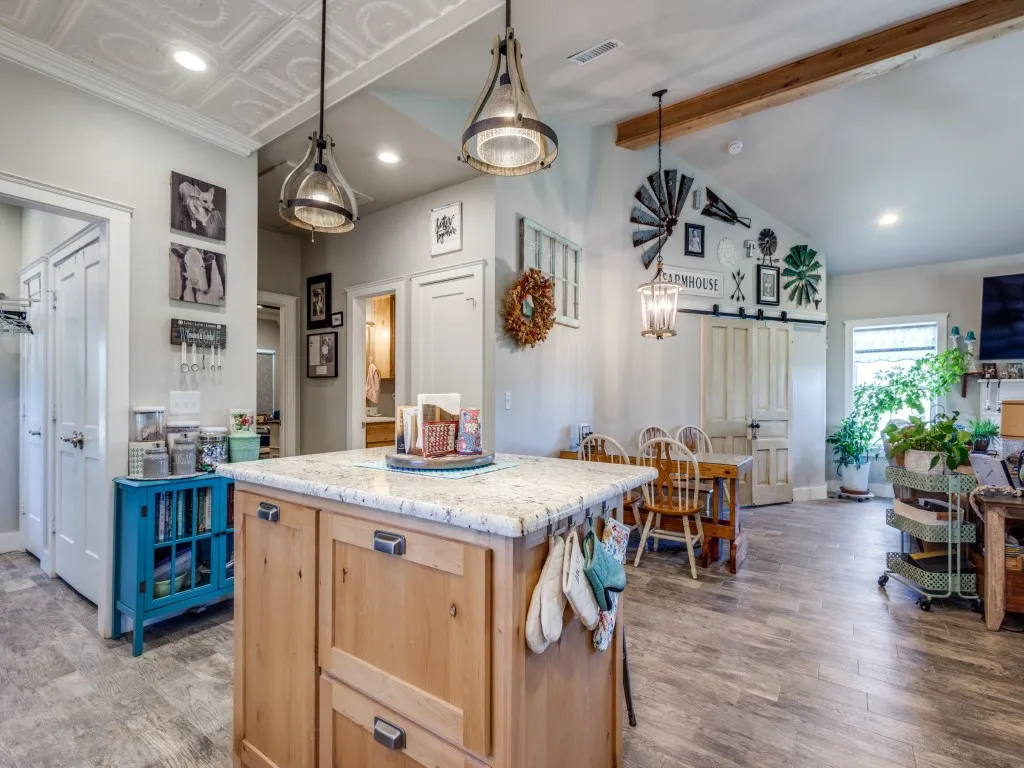 Kitchen featuring light brown cabinets, vaulted ceiling with beams, light stone counters, pendant lighting, and light wood-type flooring