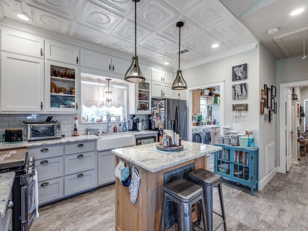 Kitchen with appliances with stainless steel finishes, a center island, backsplash, decorative light fixtures, and light stone countertops