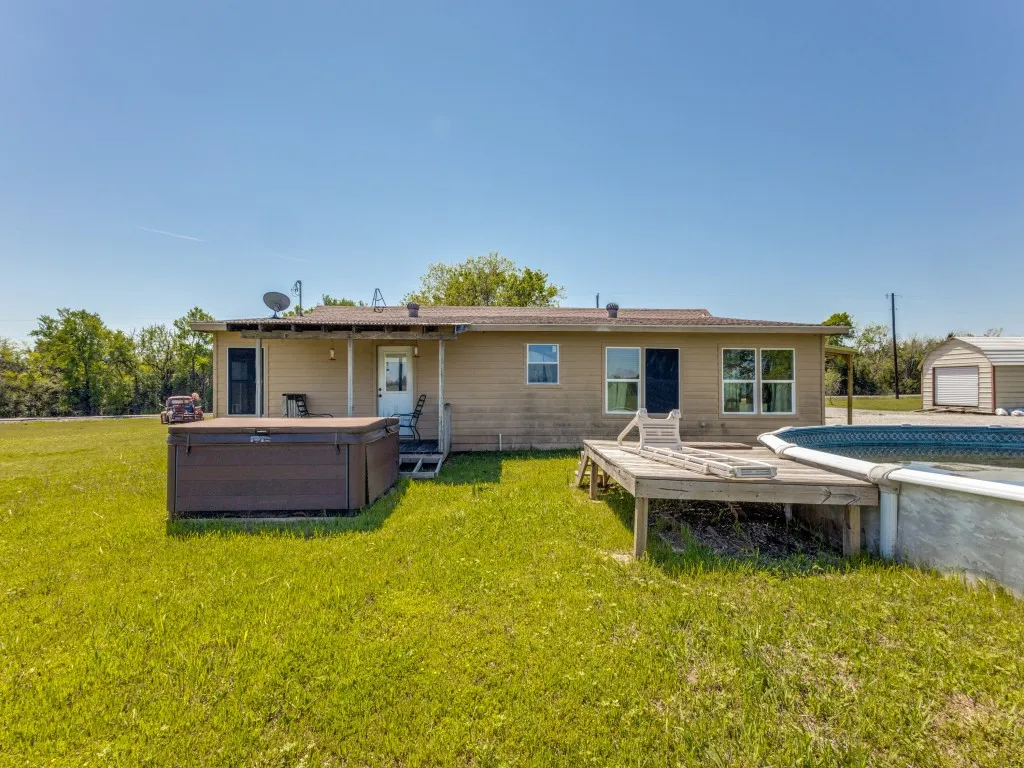 Rear view of property featuring a deck, a lawn, a hot tub, and an outdoor structure