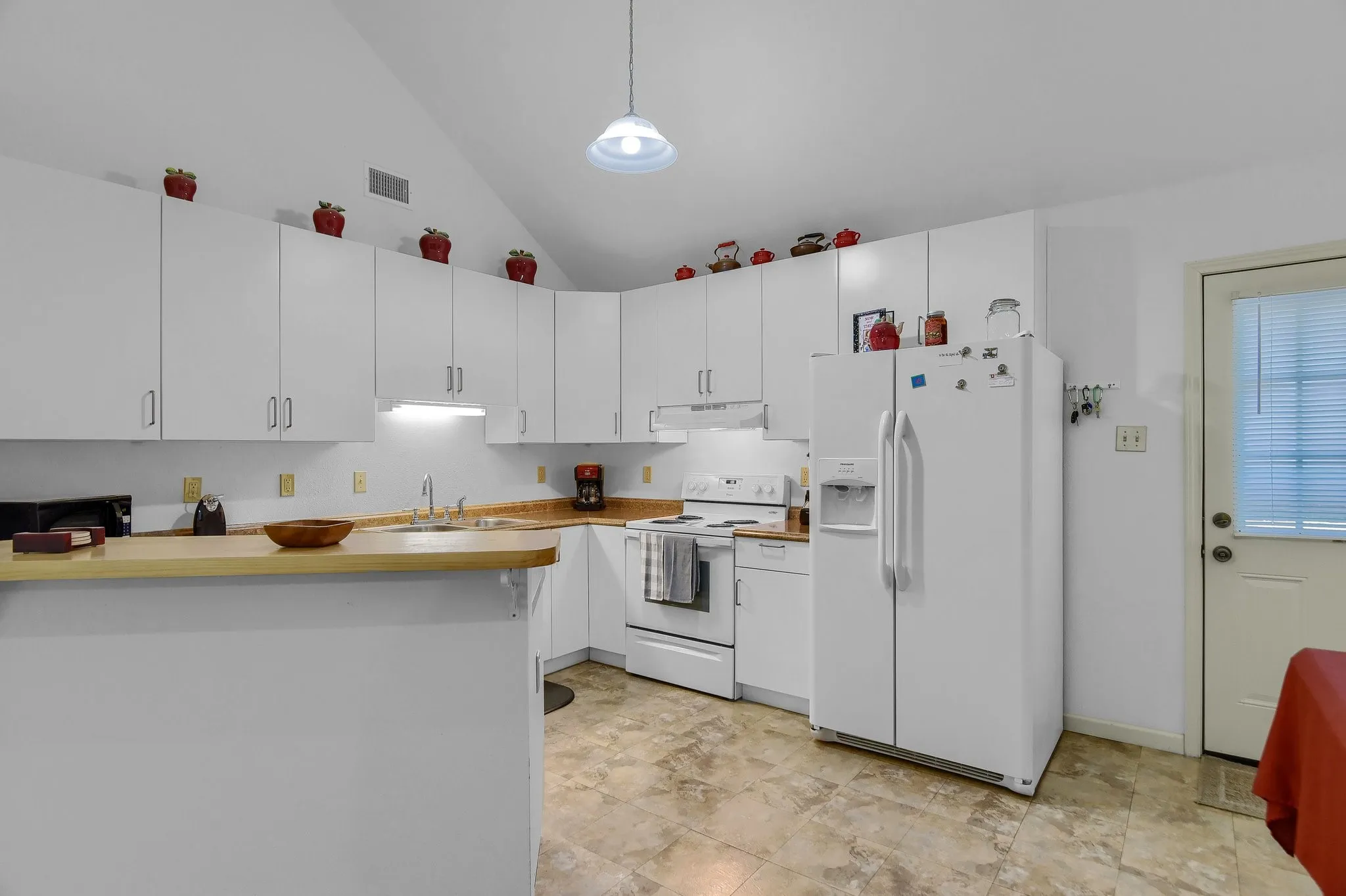 Kitchen with range hood, light tile flooring, white appliances, white cabinets, and sink