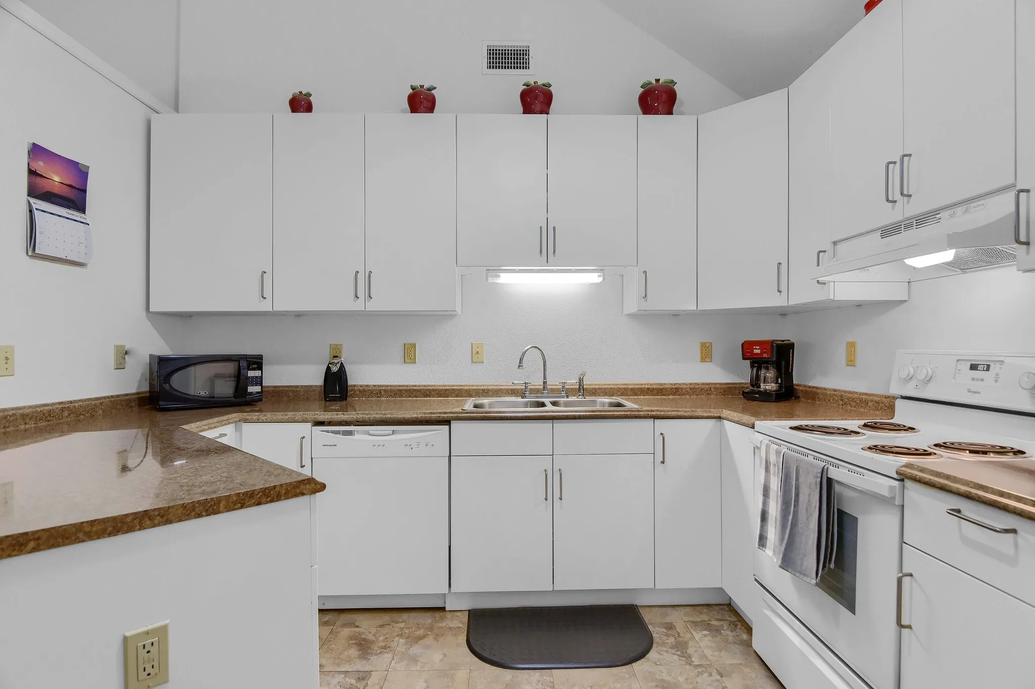 Kitchen with white appliances, sink, light tile floors, dark stone countertops, and white cabinets