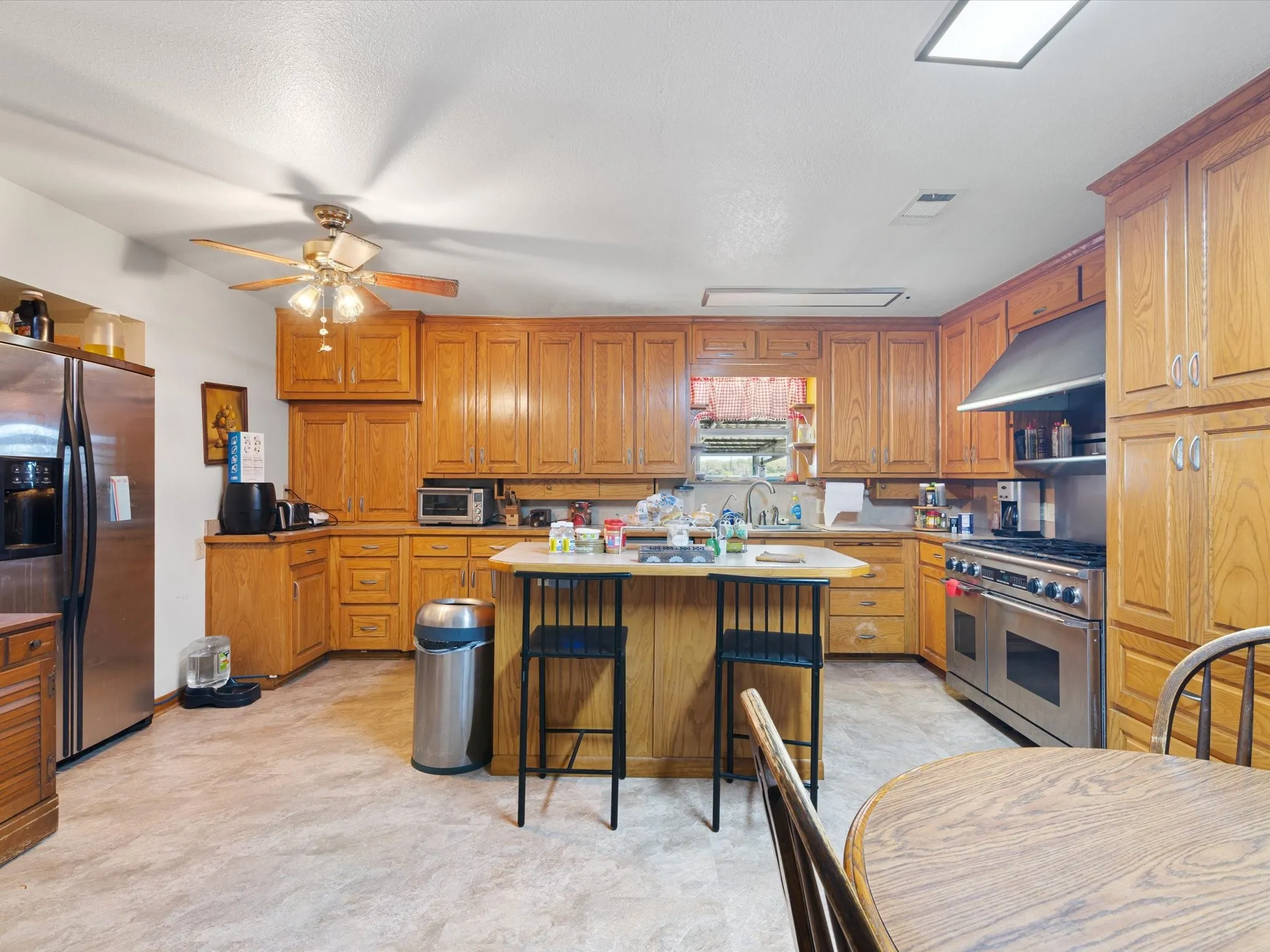 Kitchen featuring a breakfast bar, stainless steel appliances, a center island, ceiling fan, and wall chimney range hood
