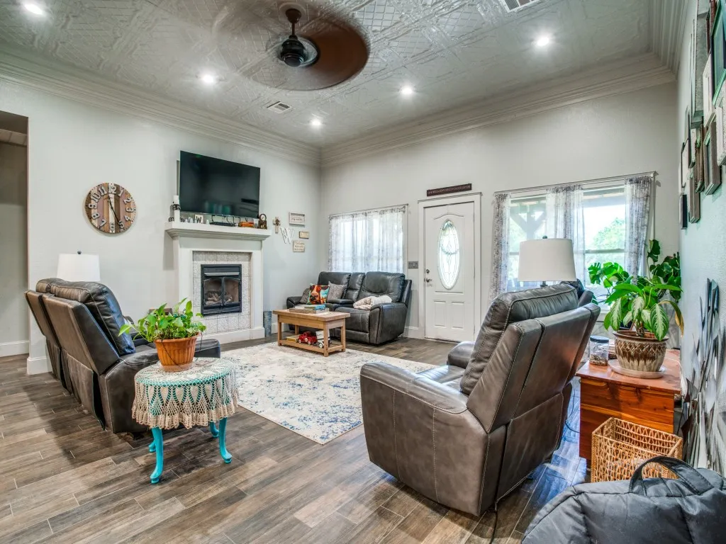 Main house living room featuring ornamental molding, wood-type flooring, ceiling fan, tiled fireplace, and stamped tin ceiling
