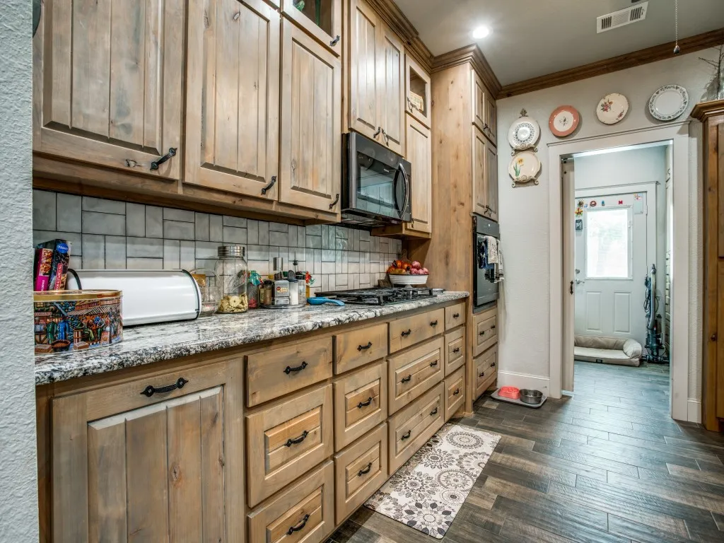 Main house kitchen featuring dark hardwood / wood-style floors, backsplash, ornamental molding, stainless steel appliances, and light stone counters
