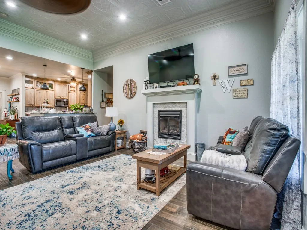 Main house living room featuring ornamental molding, wood-type flooring, ceiling fan, tiled fireplace, and stamped tin ceiling