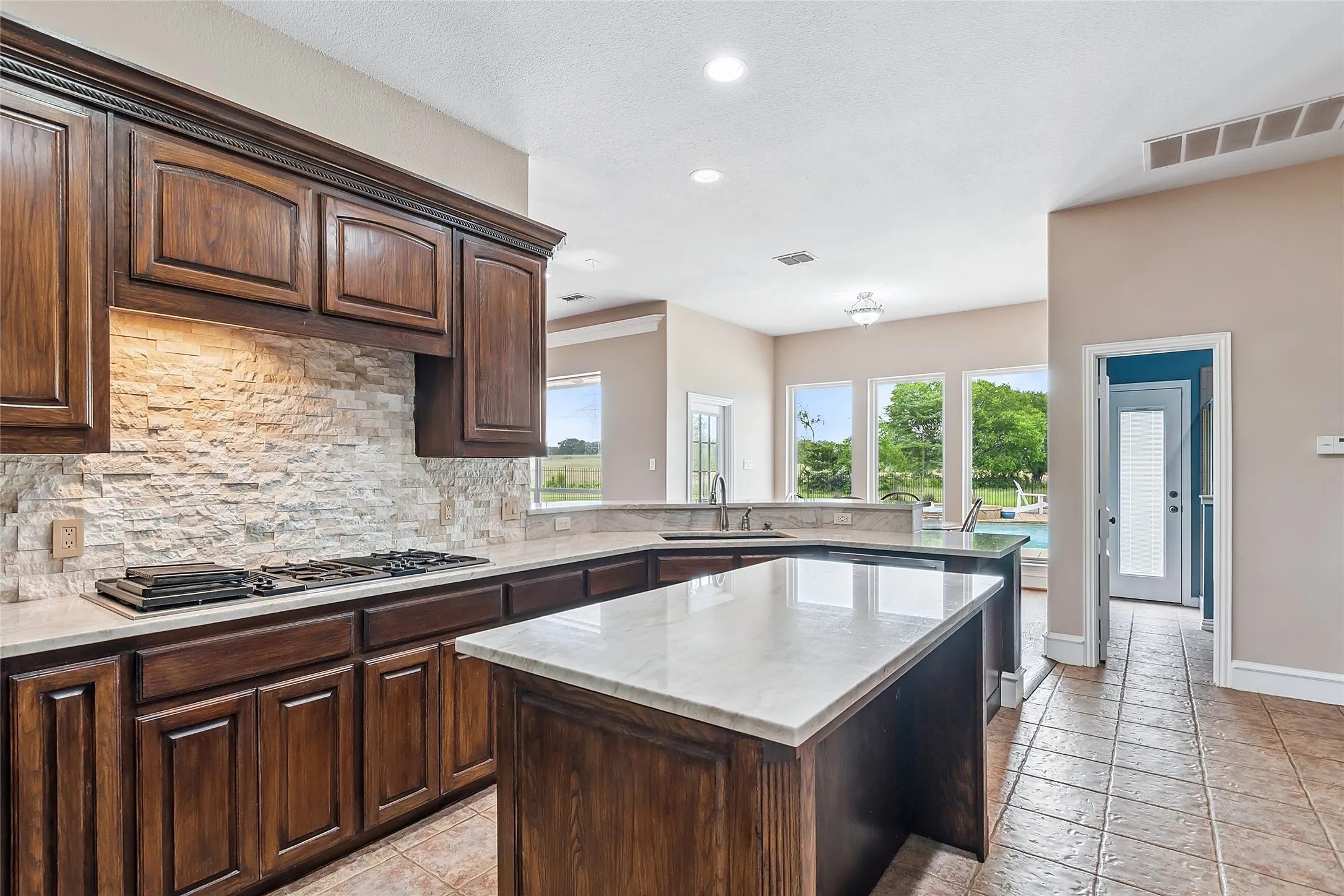 Kitchen with dark brown cabinetry, a kitchen island, backsplash, sink, and light tile floors