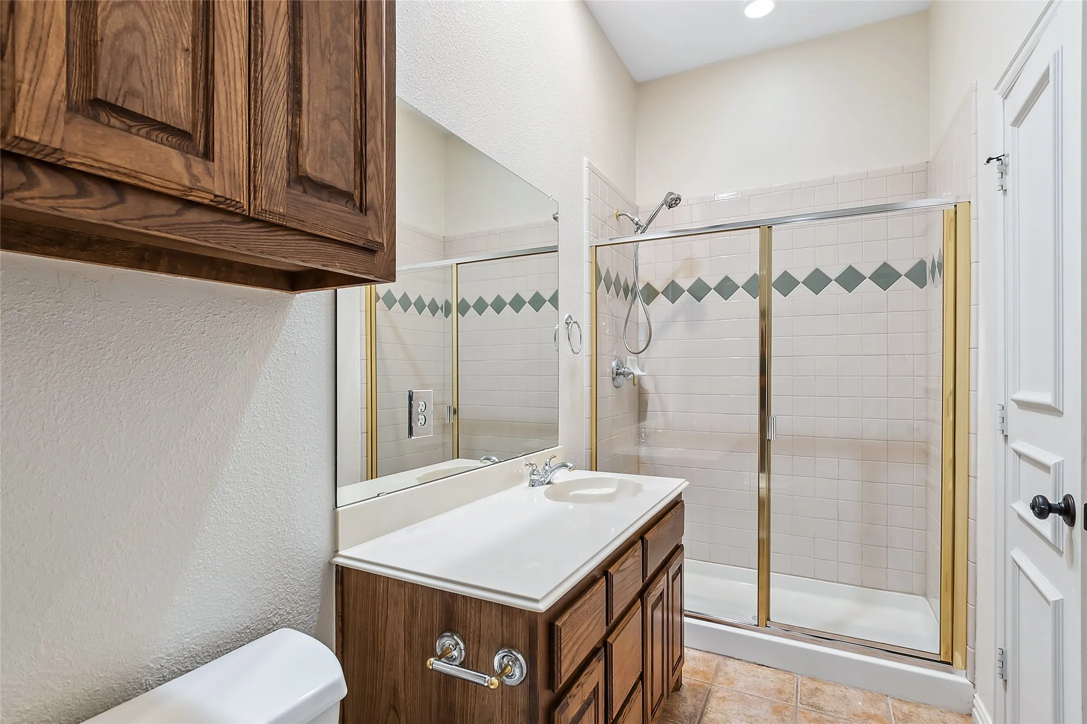 Bathroom with a shower with shower door, vanity with extensive cabinet space, toilet, and tile floors
