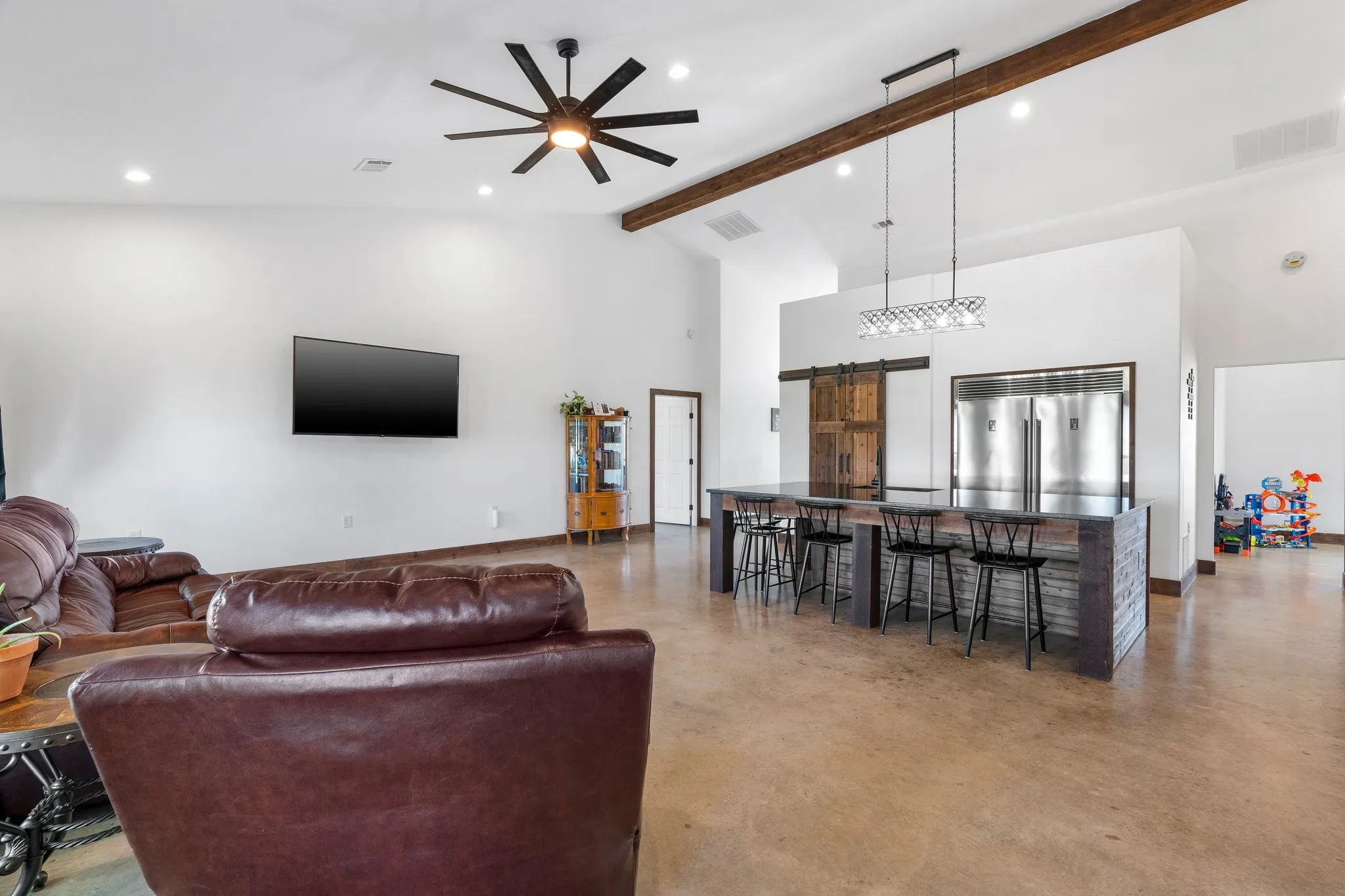 Living room with high vaulted ceiling, beamed ceiling, a barn door, and ceiling fan