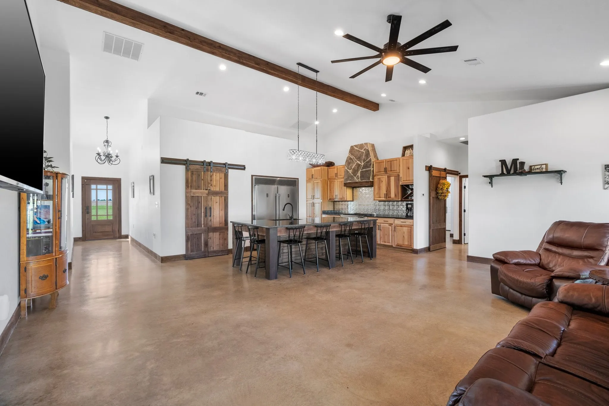Living room featuring a barn door, high vaulted ceiling, ceiling fan with notable chandelier, and beamed ceiling