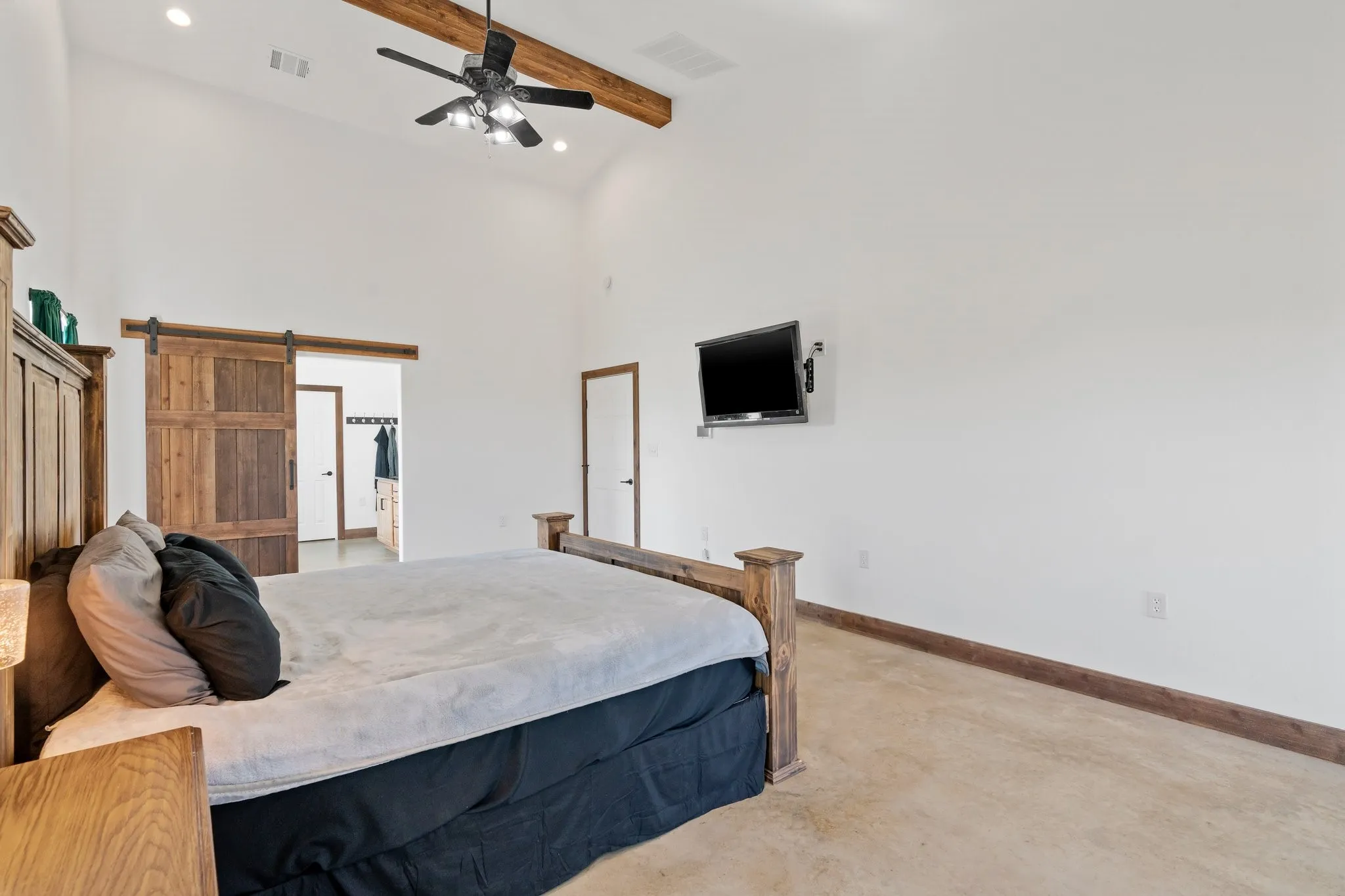 Bedroom with beamed ceiling, a barn door, a towering ceiling, carpet, and ceiling fan