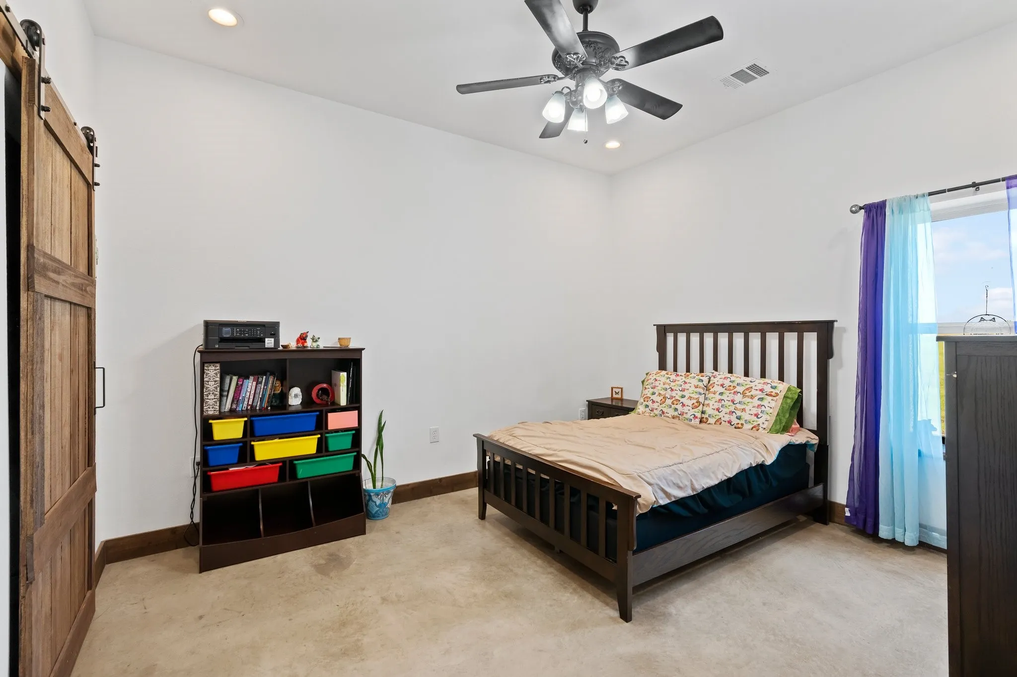 Carpeted bedroom with a barn door and ceiling fan