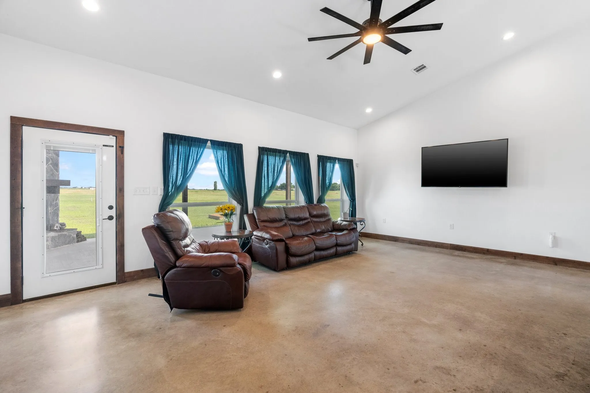 Living room featuring lofted ceiling, ceiling fan, and concrete flooring