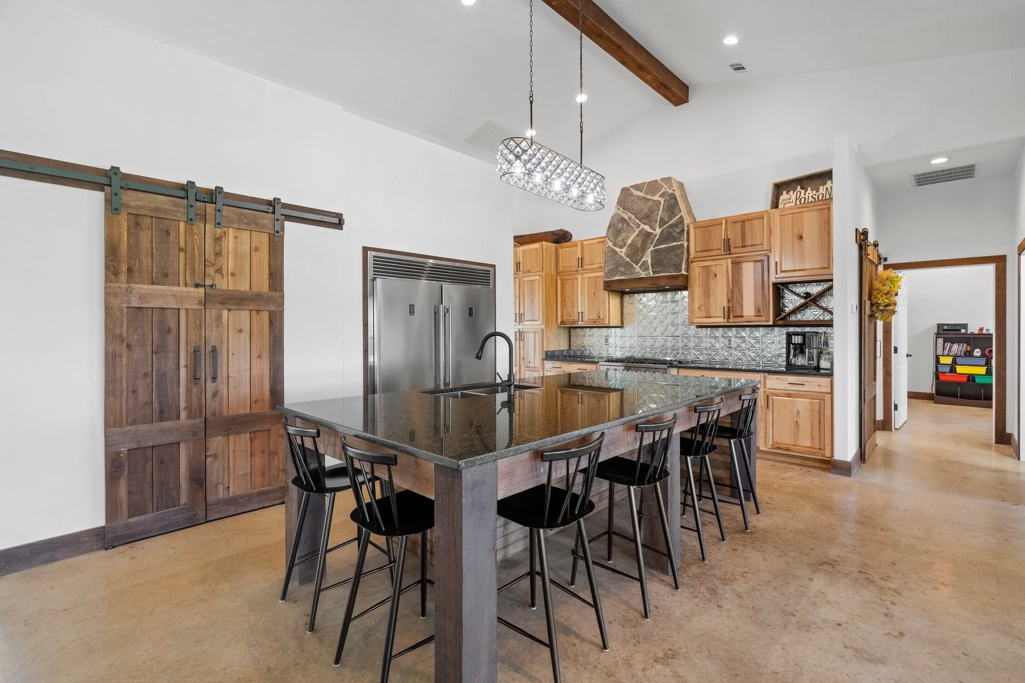 Kitchen featuring tasteful backsplash, an island with sink, a barn door, beamed ceiling, and built in refrigerator
