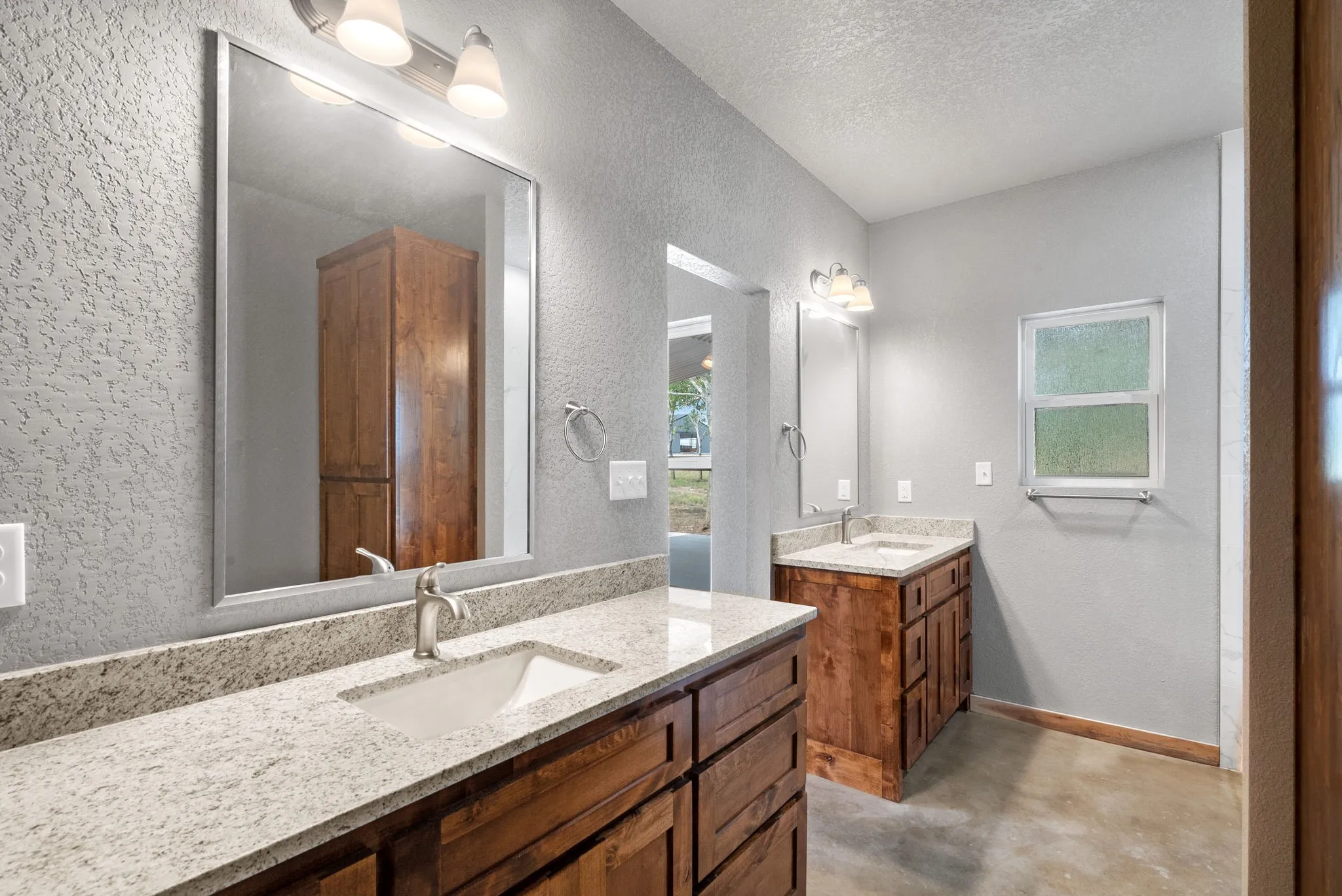 Bathroom featuring vanity with extensive cabinet space, double sink, a textured ceiling, and concrete flooring
